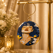 Round blue illustrated clutch bag with gold-tone chain and dangling portrait charm