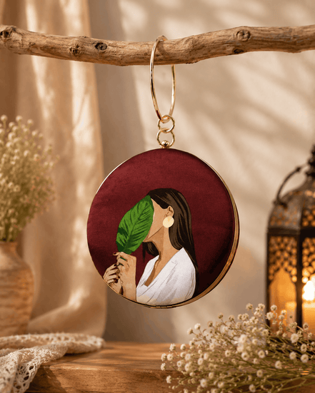 Round maroon illustrated clutch bag with gold-tone chain and leaf portrait front