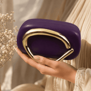 Purple clutch with gold-toned curved handle, held in hand.
