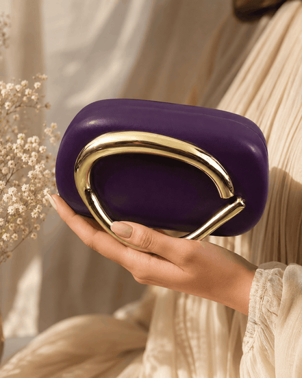 Purple clutch with gold-toned curved handle, held in hand.