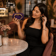 Purple clutch with gold-toned handle and frame clasp, held at dinner table.