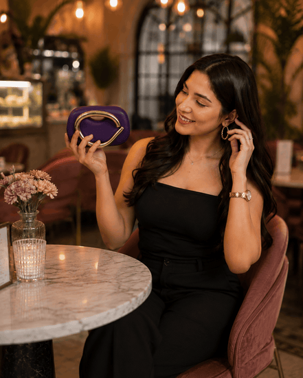 Purple clutch with gold-toned handle and frame clasp, held at dinner table.