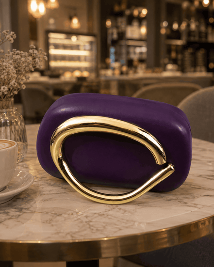 Purple clutch with curved gold-toned handle and glossy front.