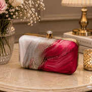Alora clutch on a table: gold-tone frame and clasp, pink and red marble design.