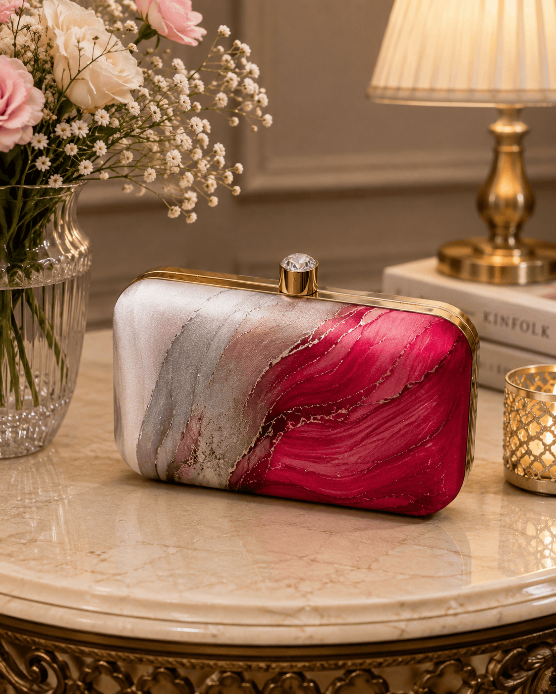 Alora clutch on a table: gold-tone frame and clasp, pink and red marble design.