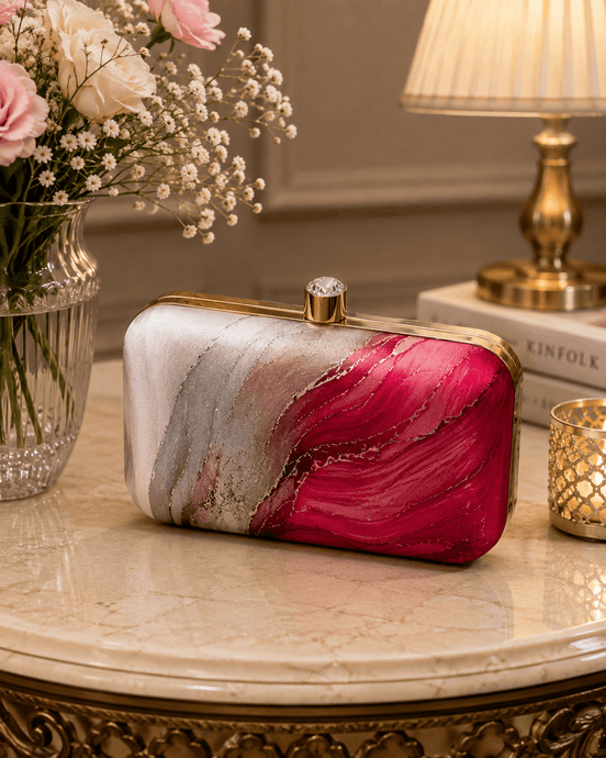 Alora clutch on a table: gold-tone frame and clasp, pink and red marble design.