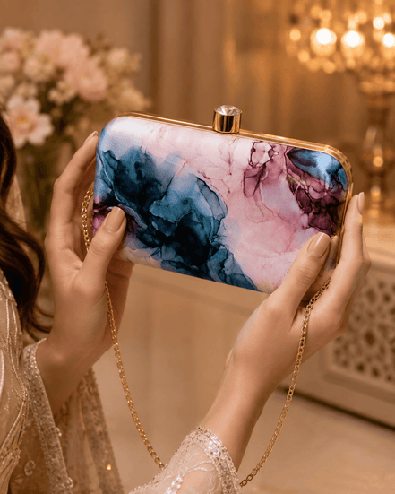 Alora clutch close-up held with hands: gold-tone frame, blue and pink marble print.