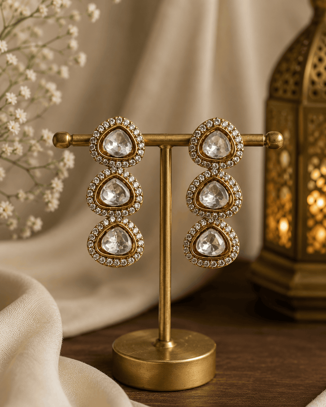 Gold-tone triple drop earrings with clear stones on a display stand