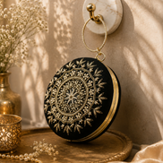 Black embroidered circular ring clutch with gold-toned floral detailing and ring handle.