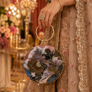 Multicolor circular embroidered ring clutch held in hand with gold-toned ring handle.