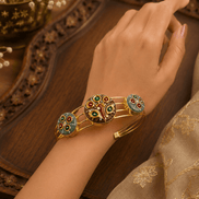 Gold-tone cuff bracelet worn on wrist, featuring colorful peacock and round enamel charms