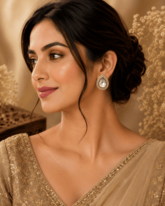 Teardrop stud earrings, gold-tone with clear crystal bezel, worn on model’s ear