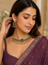 Green kundan choker necklace with matching drop earrings, worn with dark purple saree.