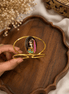 Gold-tone oval enamel face cuff bracelet with hinged open band, held in hand