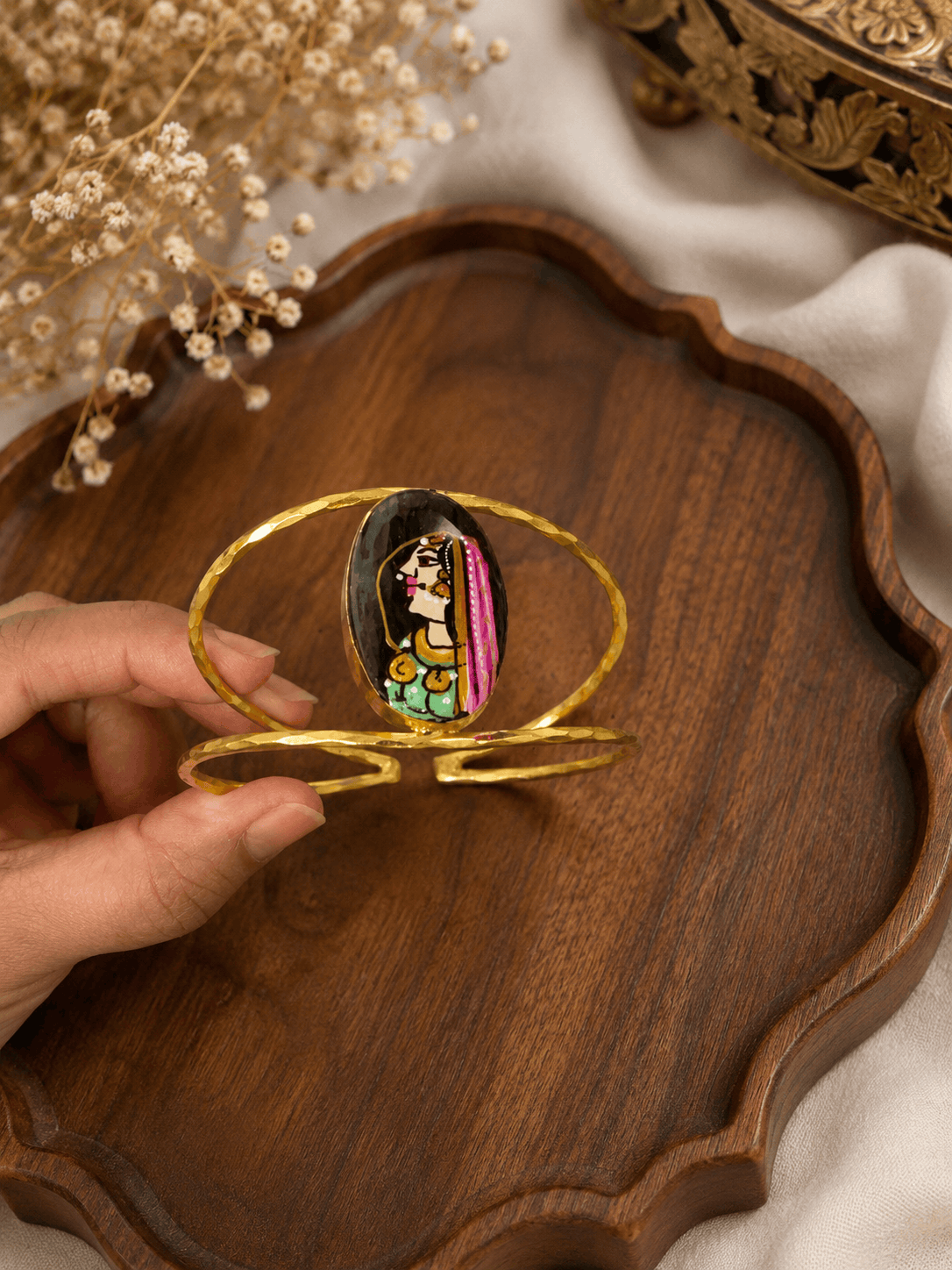 Gold-tone oval enamel face cuff bracelet with hinged open band, held in hand