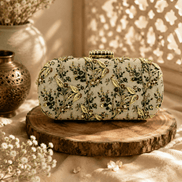 Embroidered beaded clutch bag with leafy green floral details on light fabric.