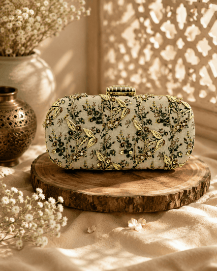 Embroidered beaded clutch bag with leafy green floral details on light fabric.