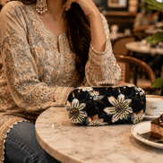Embellished black clutch bag with gold, white, and green floral applique details.