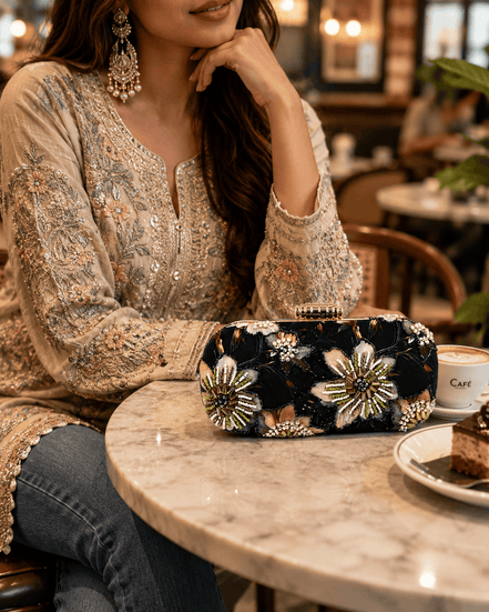 Embellished black clutch bag with gold, white, and green floral applique details.