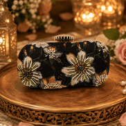 Black floral sequin clutch bag with gold and white burst embellishments, top clasp.