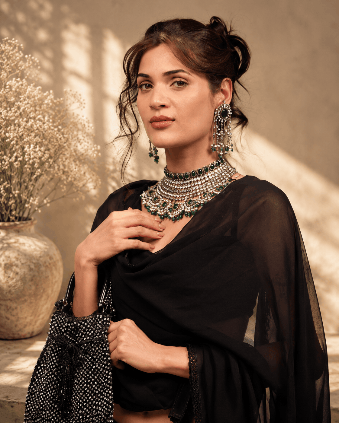 Black beaded potli bag in hand, paired with layered jewelry and a sheer drape.