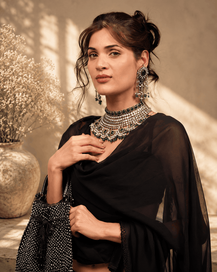 Black beaded potli bag in hand, paired with layered jewelry and a sheer drape.