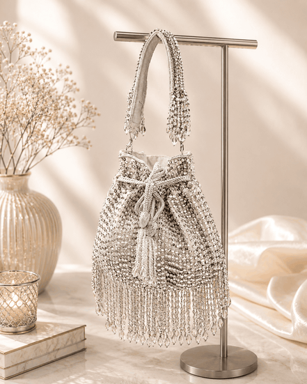 Silver beaded potli bag displayed on stand with tassel trim and drawstring.