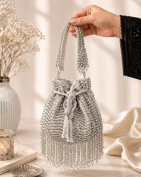 Silver beaded potli bag held up by the handle, tassels visible.