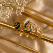 Gold-tone cuff bracelet with green and blue enamel center motif and two round black charms