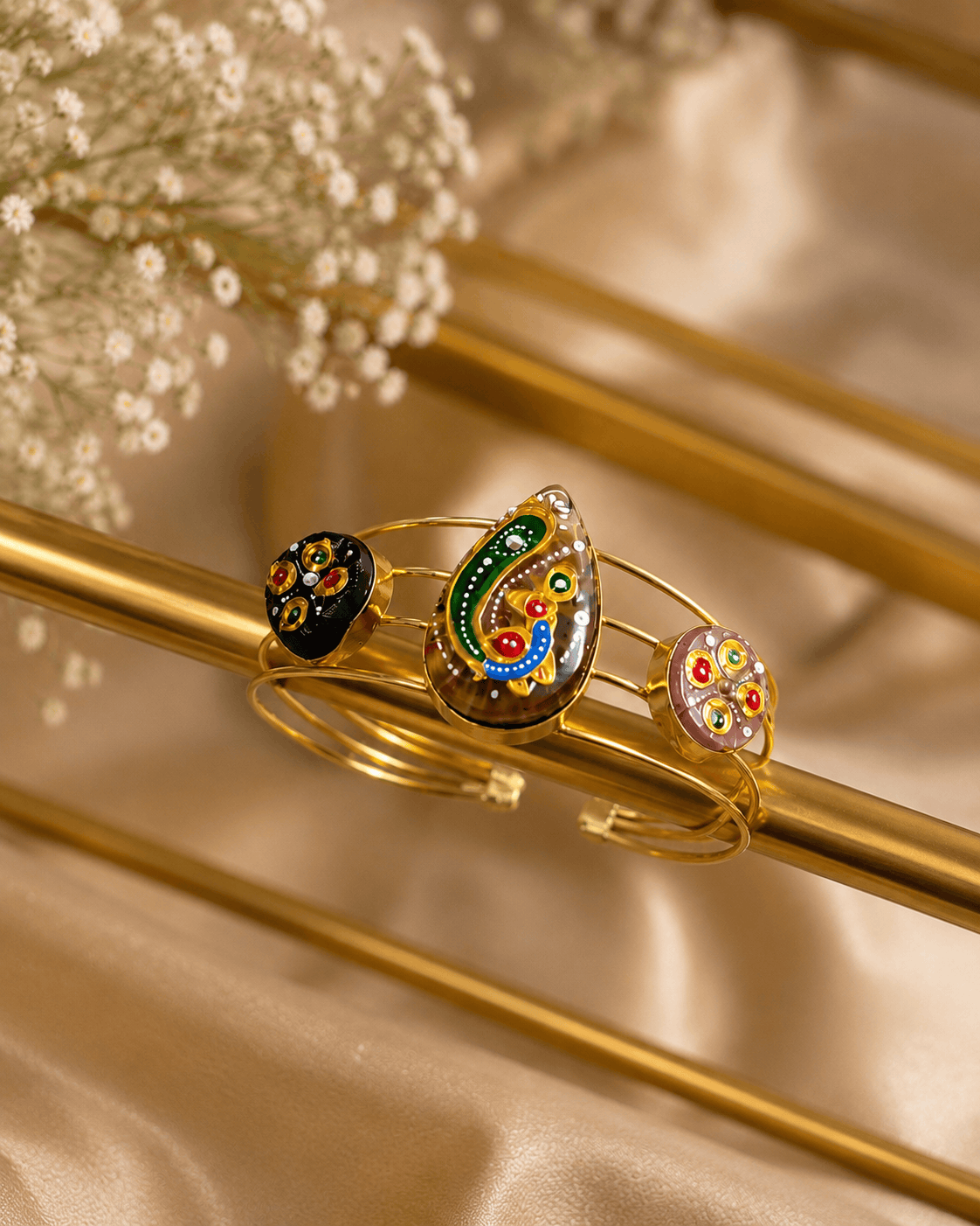 Gold-tone cuff bracelet with green and blue enamel center motif and two round black charms