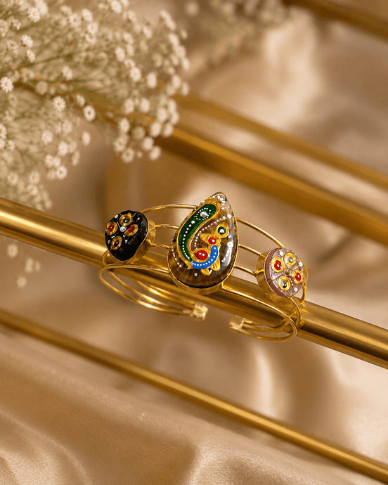 Gold-tone cuff bracelet with green and blue enamel center motif and two round black charms