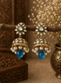 Gold-tone kundan jhumka earrings with green centers, pearl fringe, and blue drops