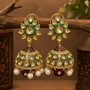 Gold-tone kundan jhumka earrings with green centers, pearl fringe, and dark red/green drops