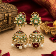 Gold-tone kundan jhumka earrings with green centers, enamel dome, and pearl fringe