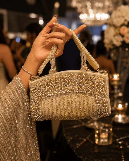 Gold-tone crystal top handle bag held by hand, with chain handle and beaded flap