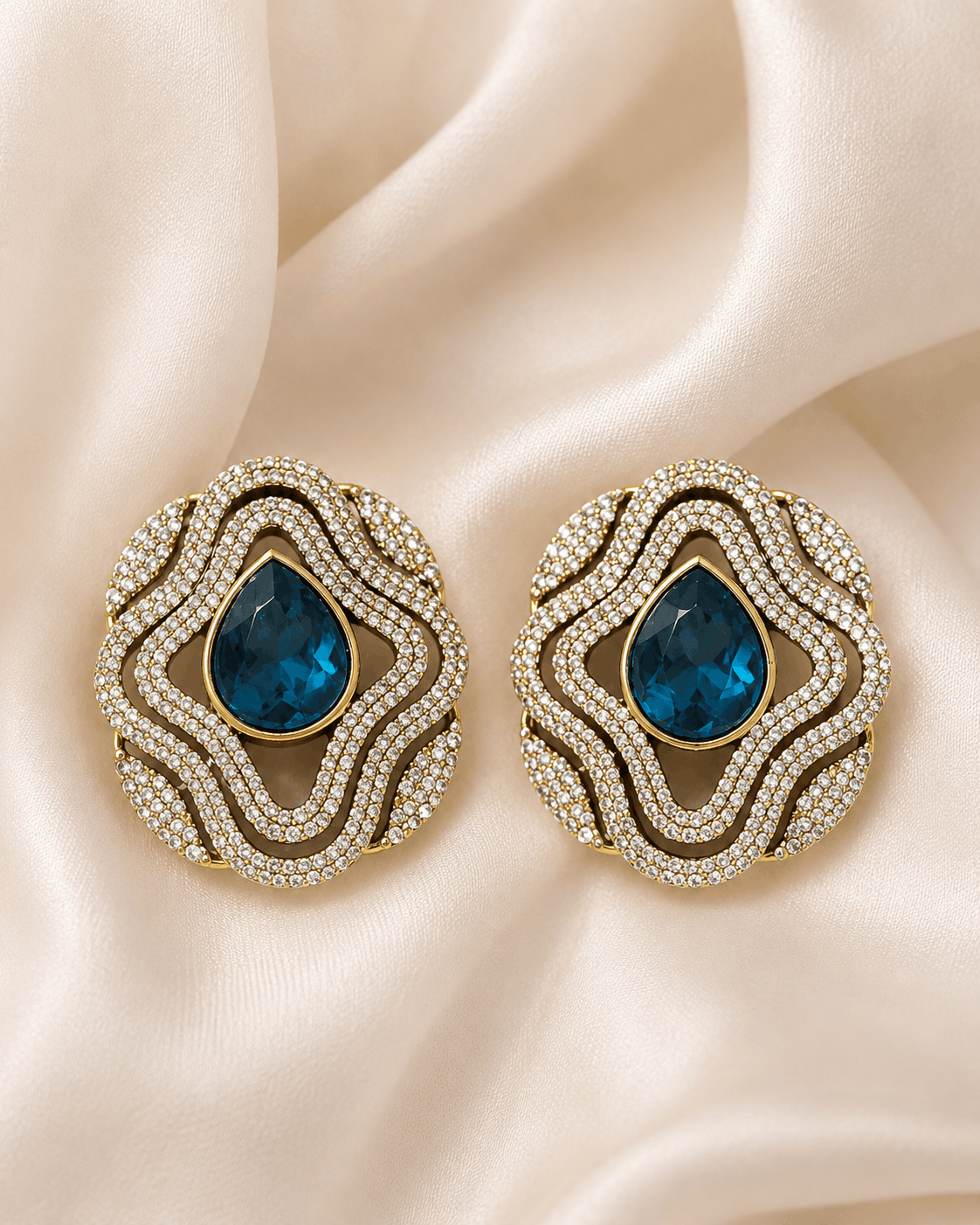 Brass-tone statement stud earrings with blue teardrop center and layered crystal trim