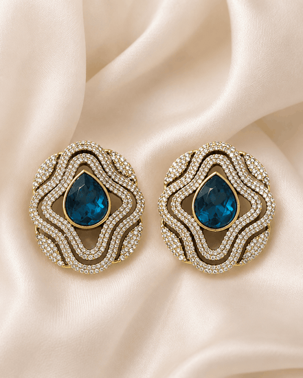 Brass-tone statement stud earrings with blue teardrop center and layered crystal trim