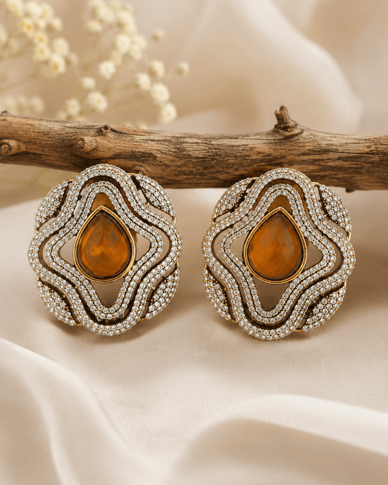 Brass-tone statement stud earrings with amber teardrop center and crystal halo border