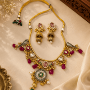 Gold-tone necklace and earring set with pink stones, green accents, and dangling charms