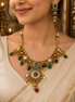 Gold-tone necklace with matching dangling earrings in green and pink stones, worn