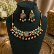Gold-tone kundan necklace set with dark green stones and red accents; matching earrings.