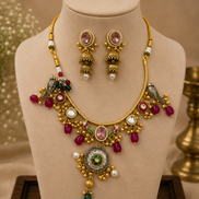 Gold-tone necklace and earring set with pink, green, and red stones on cream stand