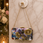 Multicolor floral clutch purse with gold-tone clasp and chain strap on marble surface
