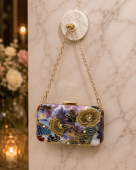 Multicolor floral clutch purse with gold-tone clasp and chain strap on marble surface