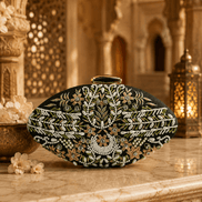 Embellished oval clutch with green beads and gold clasp on black fabric, front view
