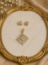 Gold-tone square crystal pendant and matching stud earrings on ornate jewelry display