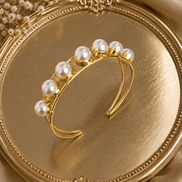 Gold-tone pearl cuff bracelet with white pearl cluster on display tray