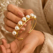 Gold-tone pearl cuff bracelet with clustered white pearls, close-up on hand