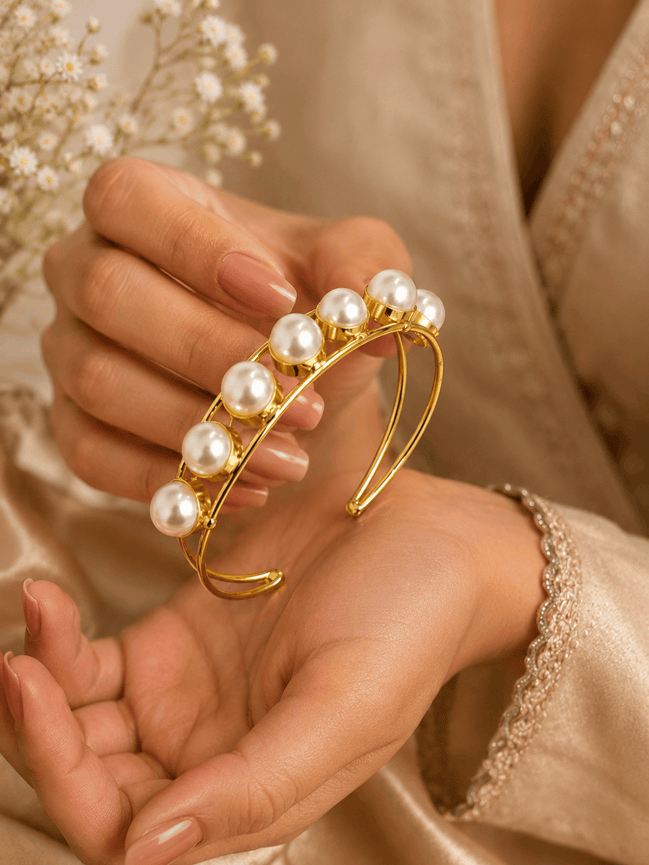 Gold-tone pearl cuff bracelet with clustered white pearls, close-up on hand