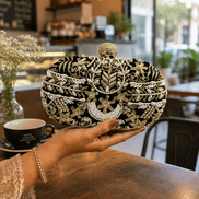 Beaded clutch with gold, black, and white embroidery; rounded top with gold clasp.